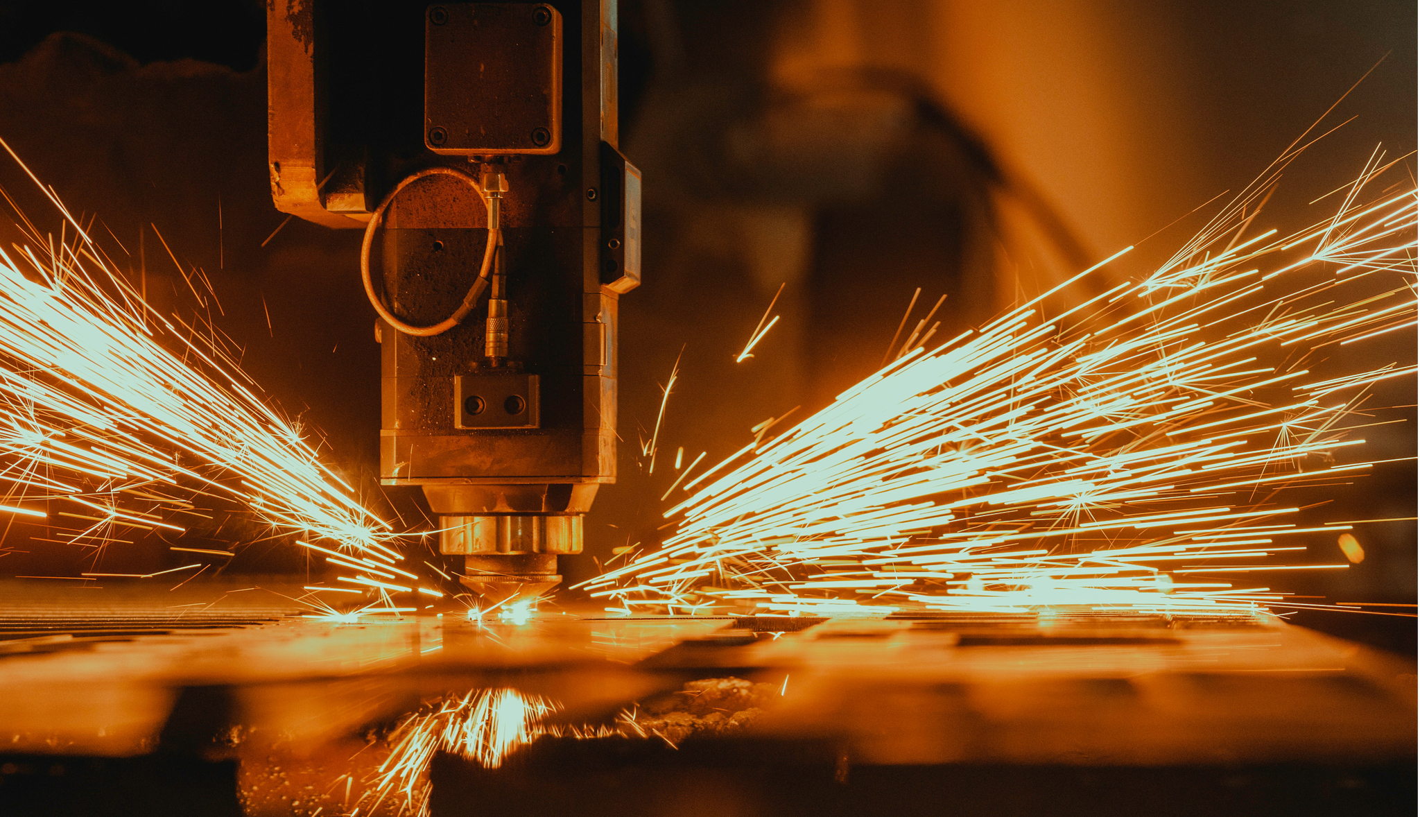 Close-up of industrial laser cutting metal, throwing long orange sparks across the work surface.